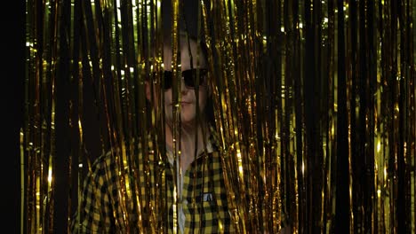 portrait of caucasian man posing on black background. gold shining foil strips. party, music, disco