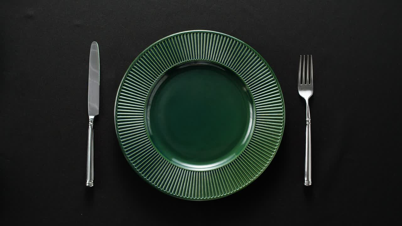 Minimalist table setting with white plate, fork, and knife arranged neatly, and a gloved hand adjusting cutlery.