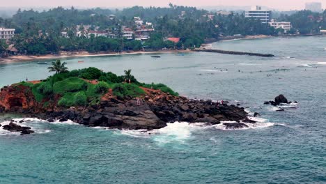 sri lanka aerial view of a rocky island with lush vegetation, surrounded by turquoise waters and gentle waves near the coastline, under slightly overcast but bright sky, captured with wide-angle lens