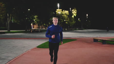 focused blond man running towards camera in the park at night