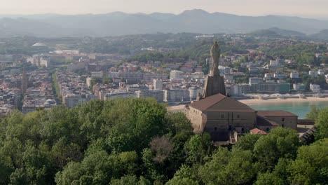 monument statue with city of san sebastian in background, cinematic aerial drone view