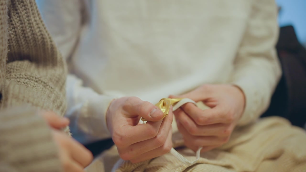 Close up of hands working with golden thread and beige knitted fabric demonstrating detailed textile craft. person manipulates material smoothly throughout calm indoor setting with soft
