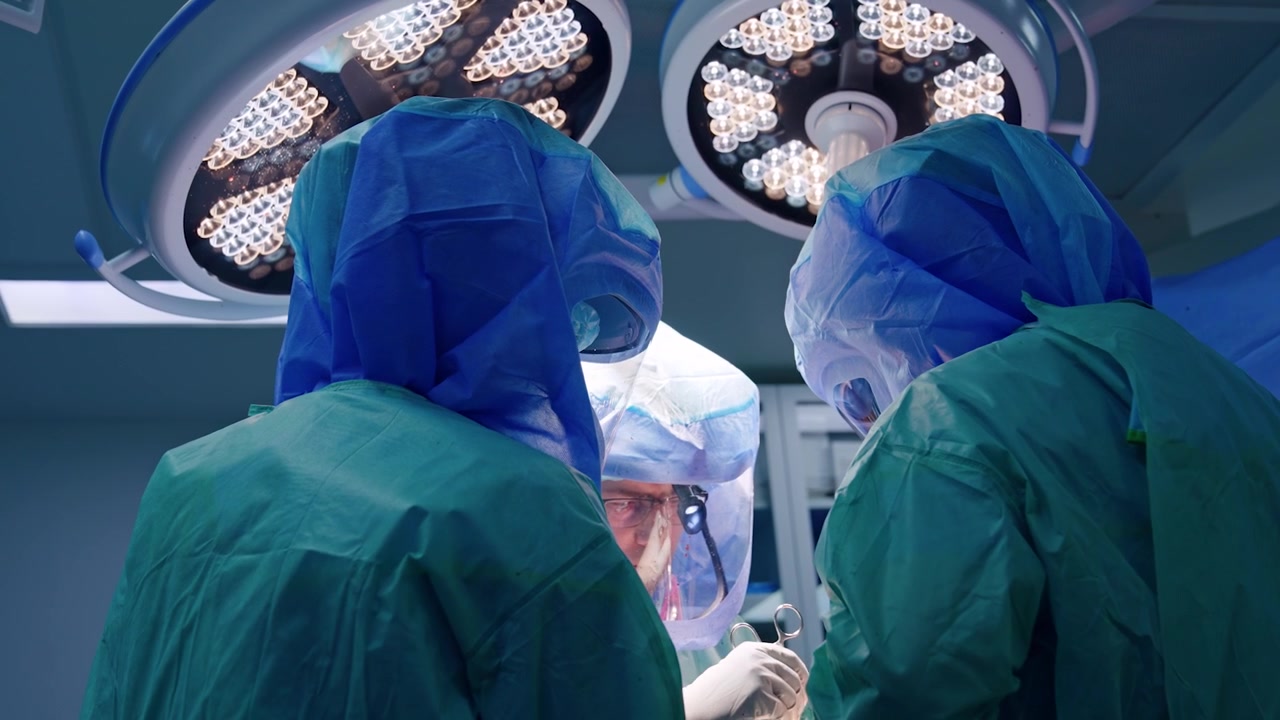 Tre chirurghi con caschi protettivi collaborano durante un'operazione. I medici usano strumenti metallici nel loro lavoro.