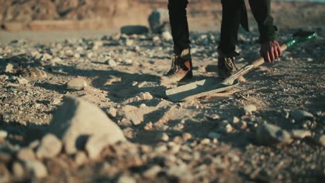 man picks up spade and starts digging into dry dusty desert soil, low angle