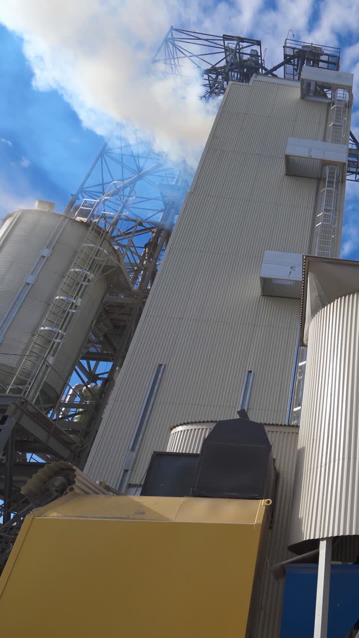 Exterior of aluminum equipment of a modern complex. Thick white smoke goes into the air from the large agricultural plant during grain processing. Vertical video