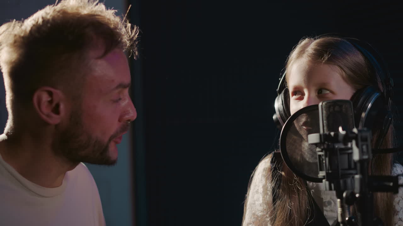 Kid with teacher sing in audio recording studio. Happy little girl improves vocal skills with professional singer in sound insulated room. Art talent