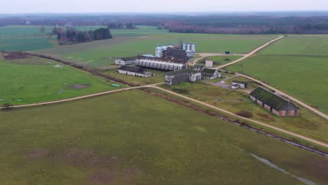 Vista-Aérea-Que-Rodea-Varios-Edificios-Agrícolas-Con-Contenedores-De-Silos-De-Acero-En-Tierras-Agrícolas-Rurales