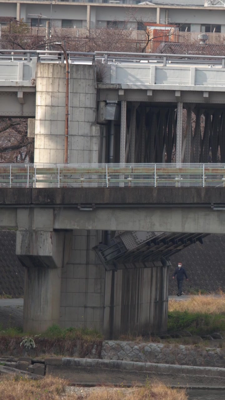 Inquadratura ampia statica di un ponte di cemento su un percorso fluviale con infrastrutture urbane.