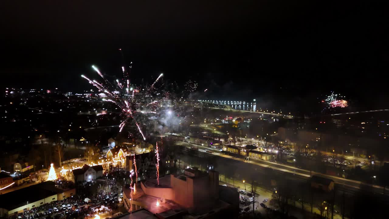 fuegos artificiales en una pequeña ciudad, explotando en una variedad de colores, incluyendo rojo, verde, azul, amarillo y naranja, contra un cielo nocturno oscuro