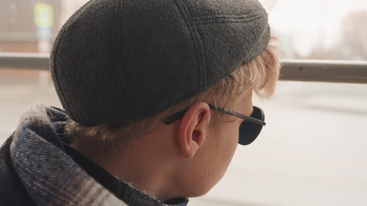 Young man staring out window, contemplative creator on urban commute, profile portrait with sunglasses and cap, soft motion blur outside, introspective cinematic mood and quiet storytelling