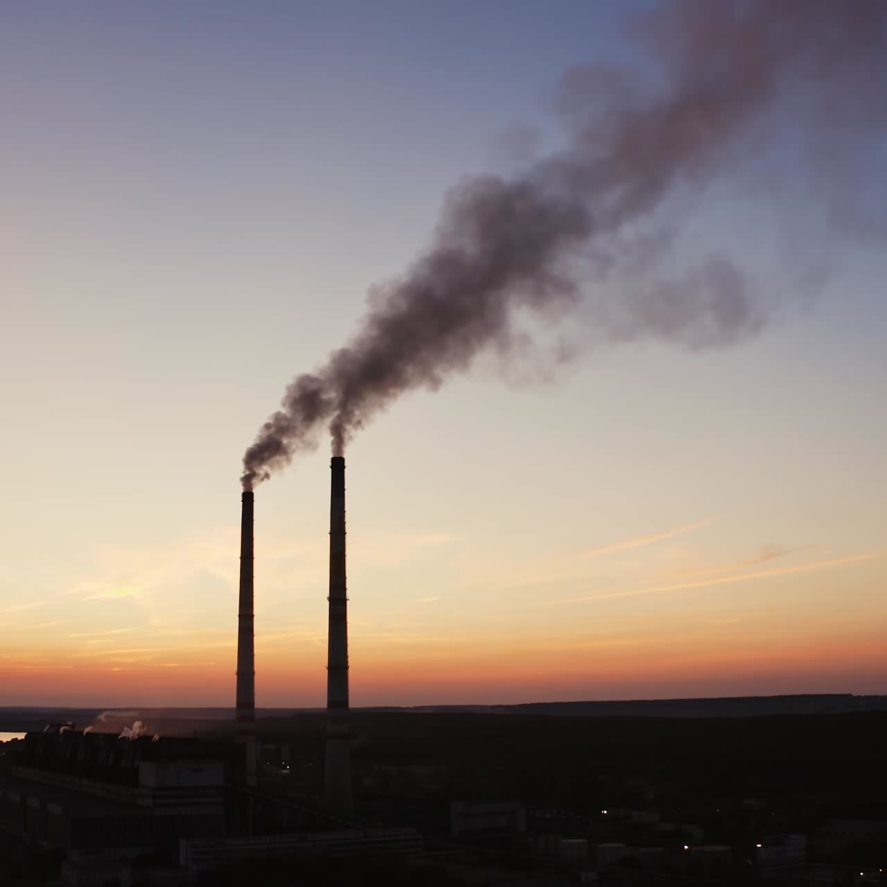 Dirty smoke from industrial pipes over the clear evening sky. Chemical smoke comes out of the pipes of power plant at darkness.