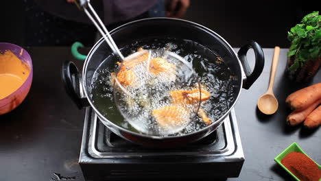 chef frying chicken lollipop in sizzling hot oil by a stainless steel deep fryer, preparing chicken lollipop