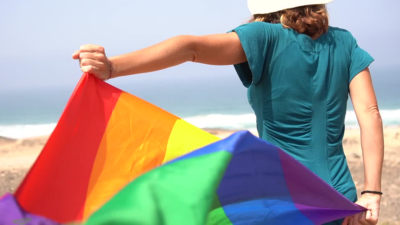 Kvinde med LGBTQ Pride regnbueflag på stranden