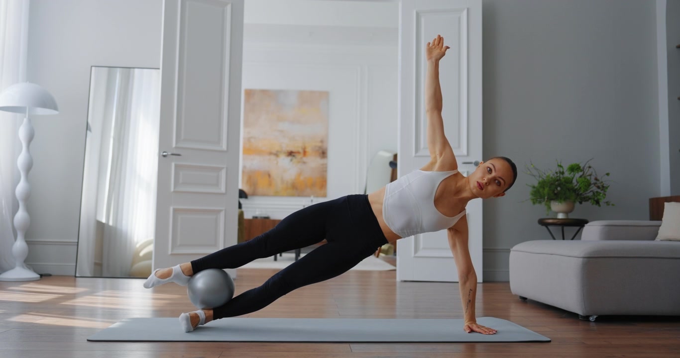 Fit Woman Performing Side Plank with Pilates Ball on Yoga Mat