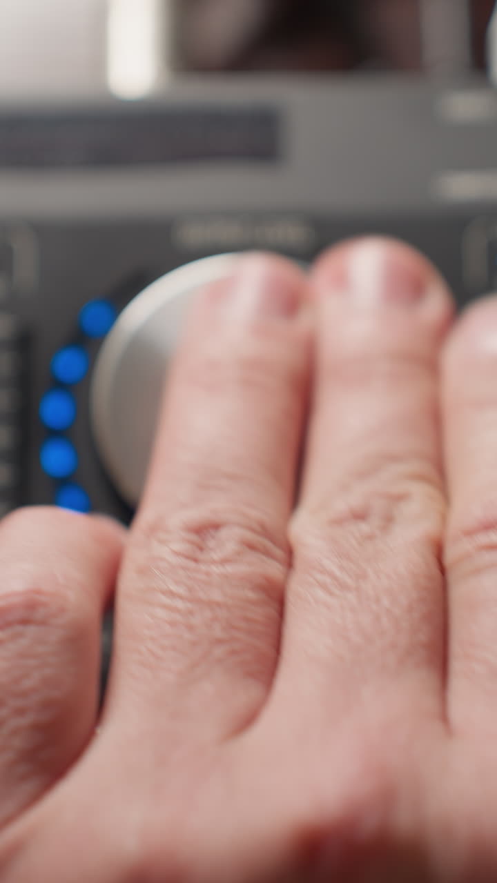 primer plano de una mano que opera un mezclador de sonido, girando una perilla hacia la izquierda para ajustar los niveles de audio. con la interfaz del mezcladora y varios controles claramente visibles