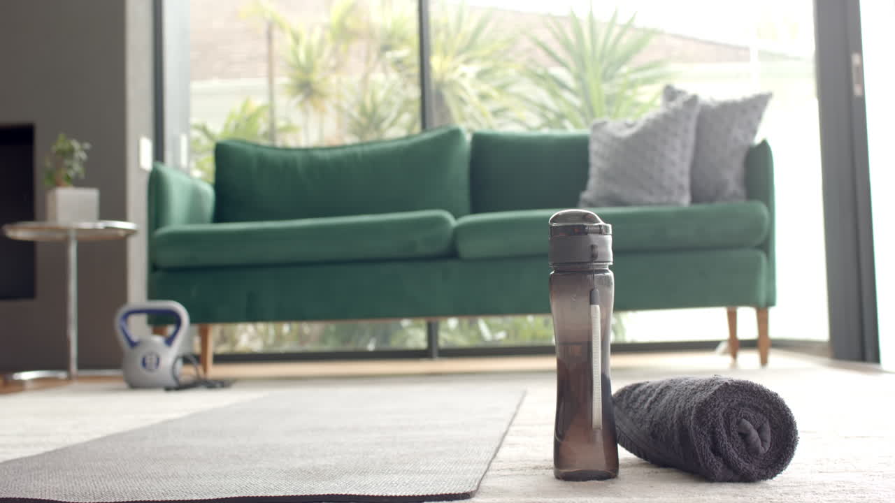 Water bottle and towel on yoga mat in living room, ready for home workout, copy space