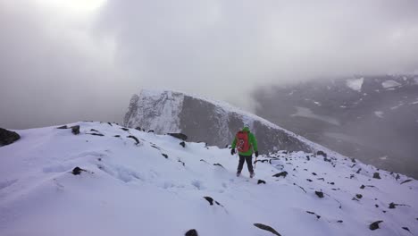 persona bajando lentamente desde la cumbre de la montaña cubierta de nieve en un clima nublado