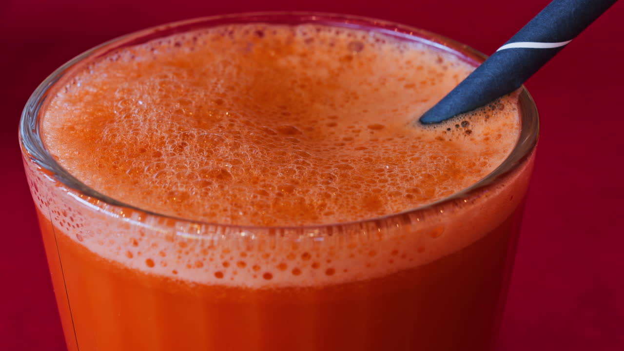 Close up of an orange and carrot juice in a glass with a black straw on a red table cloth