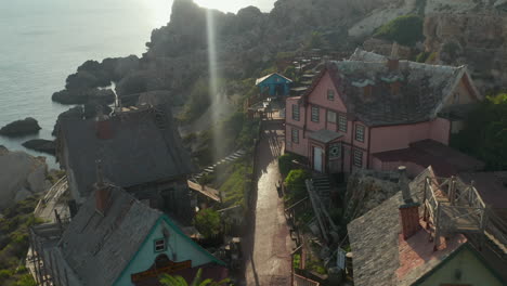 Idyllic-mediterranean-Small-Fisher-Village-with-Palm-Trees-build-by-Water-on-Rocks-with-Beautiful-Afternoon-Sunlight,-Aerial-Drone-Dolly-forward