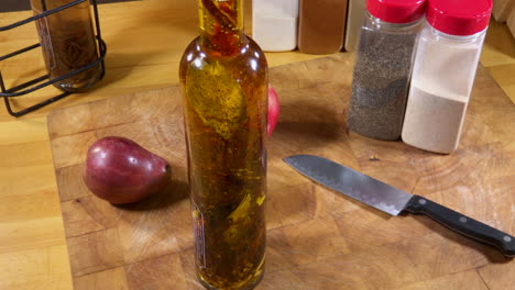 bottle of herb infused olive oil sits on cutting board with knife, fruit and spices