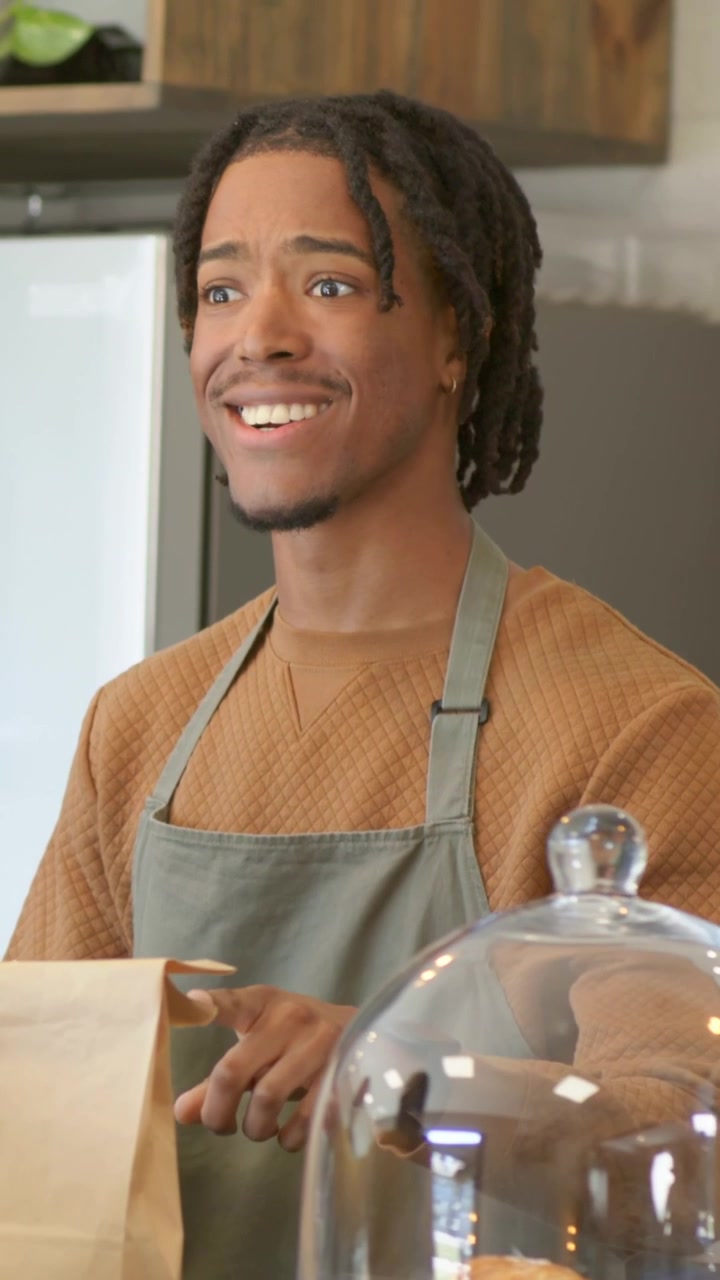 Vertical video: Taking order, worker wearing apron tapping POS packing cups bag in cafe, copy space