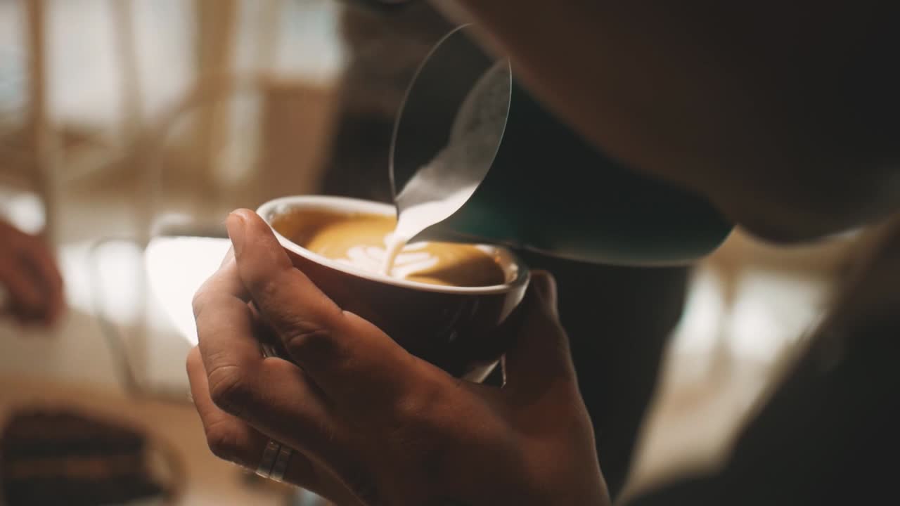 Barista pouring milk into a cappuccino.