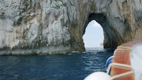 A-wooden-boat-is-approaching-to-the-famous-Capri's-Faraglioni-during-a-sunny-morning-in-spring