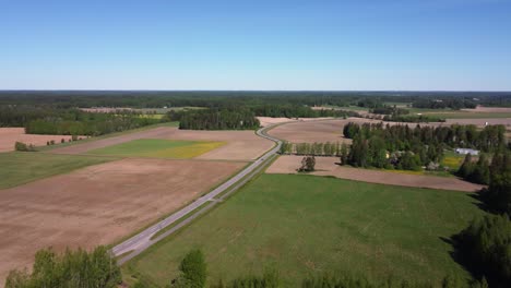 Rural-highway-winds-through-agriculture-fields,-green-northern-forest