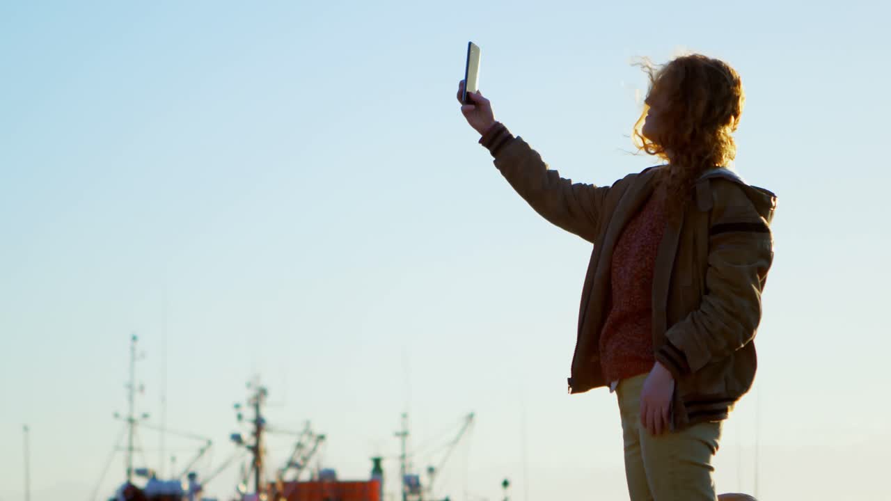 Donna che si scatta un selfie con lo smartphone al molo 4K