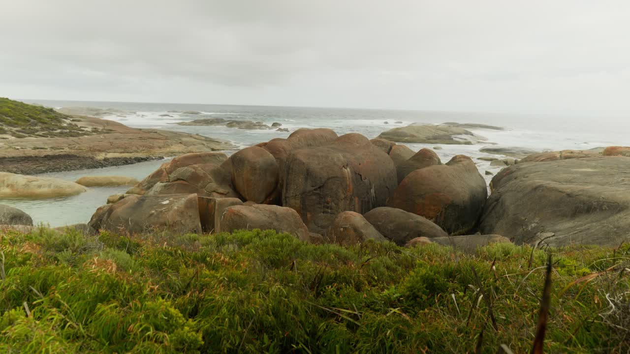 A wide shot of Elephant Rocks, featuring massive rounded boulders rising from turquoise waters, surrounded by a stunning coastal landscape and gentle ocean waves.