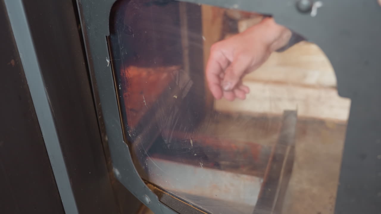 Close up of individual cleaning smoked chimney glass using tissue cloth, hand gently wipes away residue and soot, revealing firewood stacked behind glass, showing care, cleanliness, and cozy home