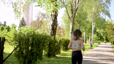 back view of a sportswoman running at the park in a sunny day while a kid riding his bike