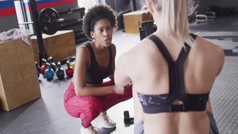 video of diverse, happy female trainer encouraging woman on rowing machine working out at a gym