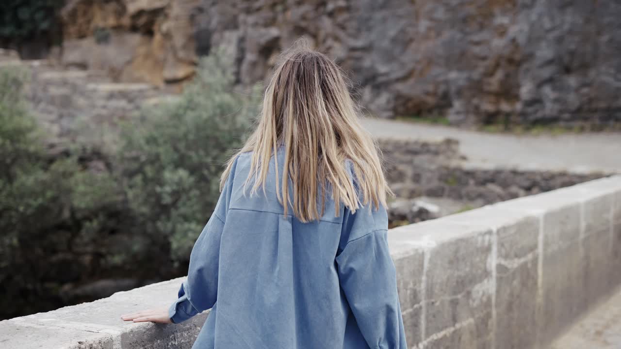 Woman tourist walks by the road bridge with view of the rocks and hills