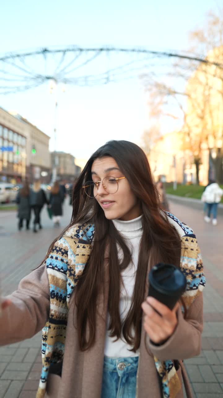 Young woman taking a selfie on the street while having coffee