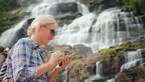 un viajero usa un teléfono inteligente contra el fondo de una cascada tvindefossen en noruega 4k video