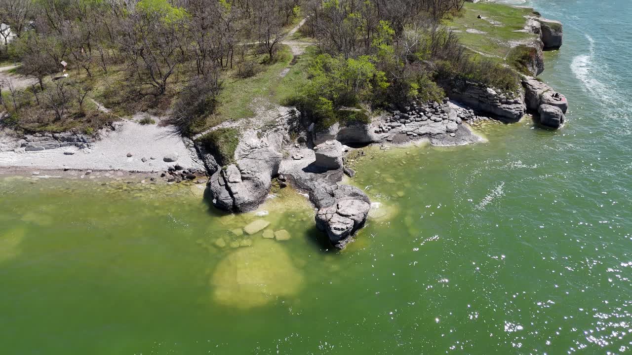 Güneşli bir yaz gününde Manitoba Gölü'nün plajını, ağaçlarını ve yeşil suyunu gösteren Steep Rock Manitoba'daki kireçtaşı kayalıklarına kilitlenmiş halde yükselen drone
