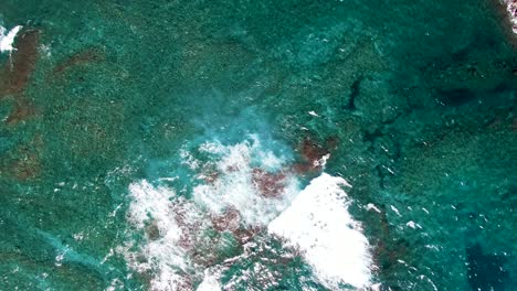 waves wash over rocks in shallow turquoise water, overhead aerial