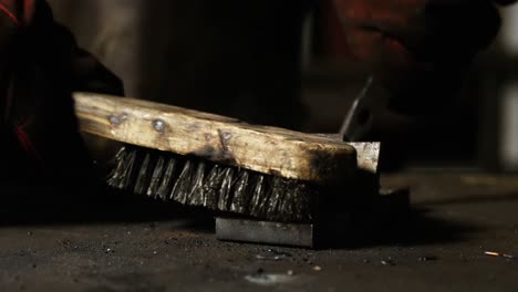 las manos del soldador usando un pincel de alambre en una pieza de metal