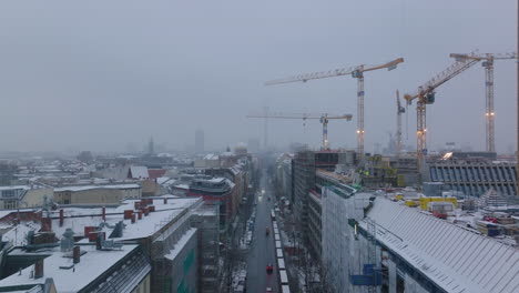 Backwards-reveal-of-street-in-town.-Construction-site-with-tall-tower-cranes-on-side.-Winter-weather-in-city.-Berlin,-Germany