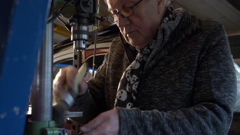 senior metal worker cleaning and preparing drilling machine in a small dark workshop