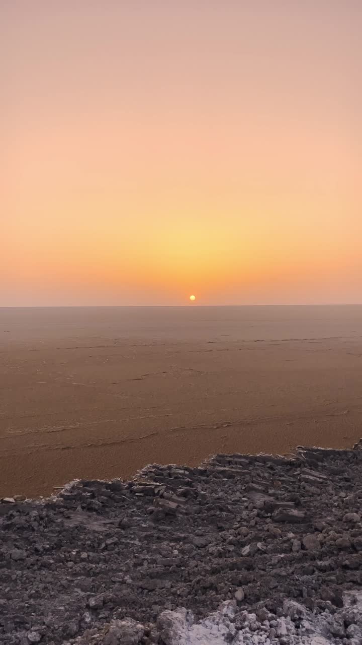 An endless stretch of the white Rann of Kutch glows under a stunning sunset of orange and pink hues, as a rocky path winds through the surreal salt desert in Gujarat, India