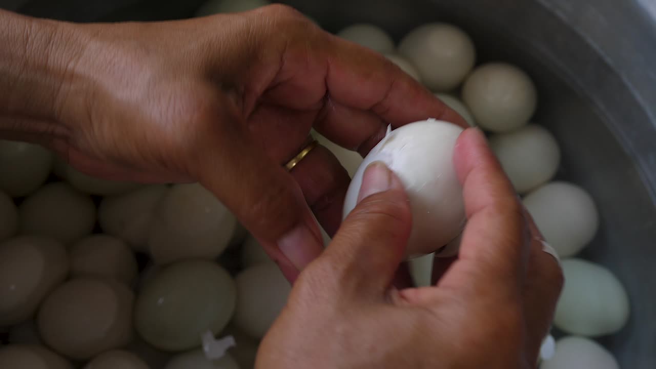 Hand peeling hard boiled duck eggs over pot of water, close up