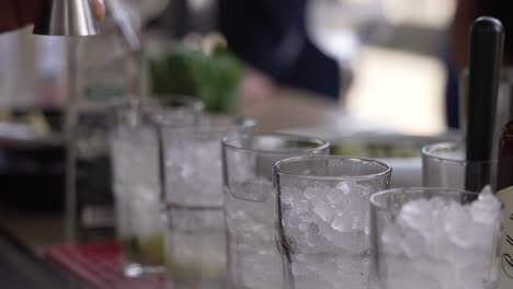 Bartender-adding-liquid-to-iced-glasses-at-a-bar,-preparing-cocktails-with-mint-and-lime