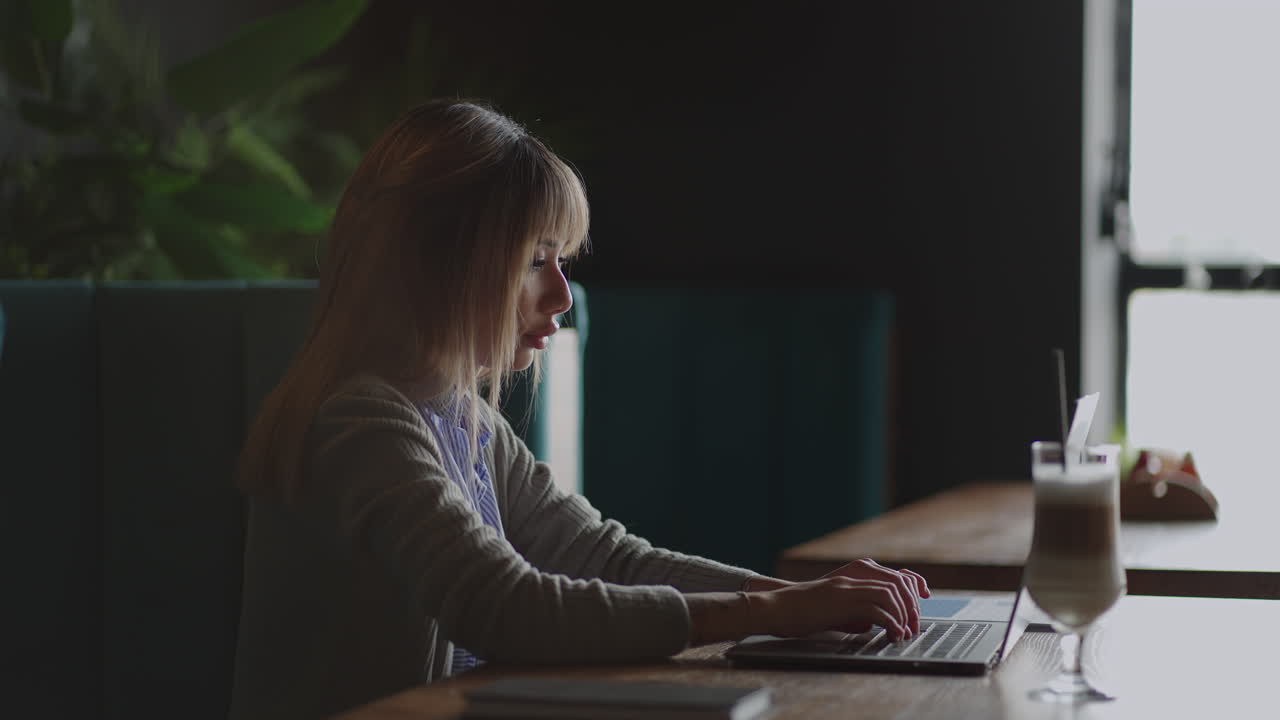 Young Asian attractive female office worker sitting at a coffee shop at the laptop computer at the desk working and thinking.