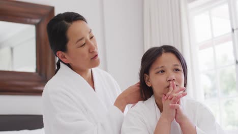 video of happy asian mother and daughter in robes having fun