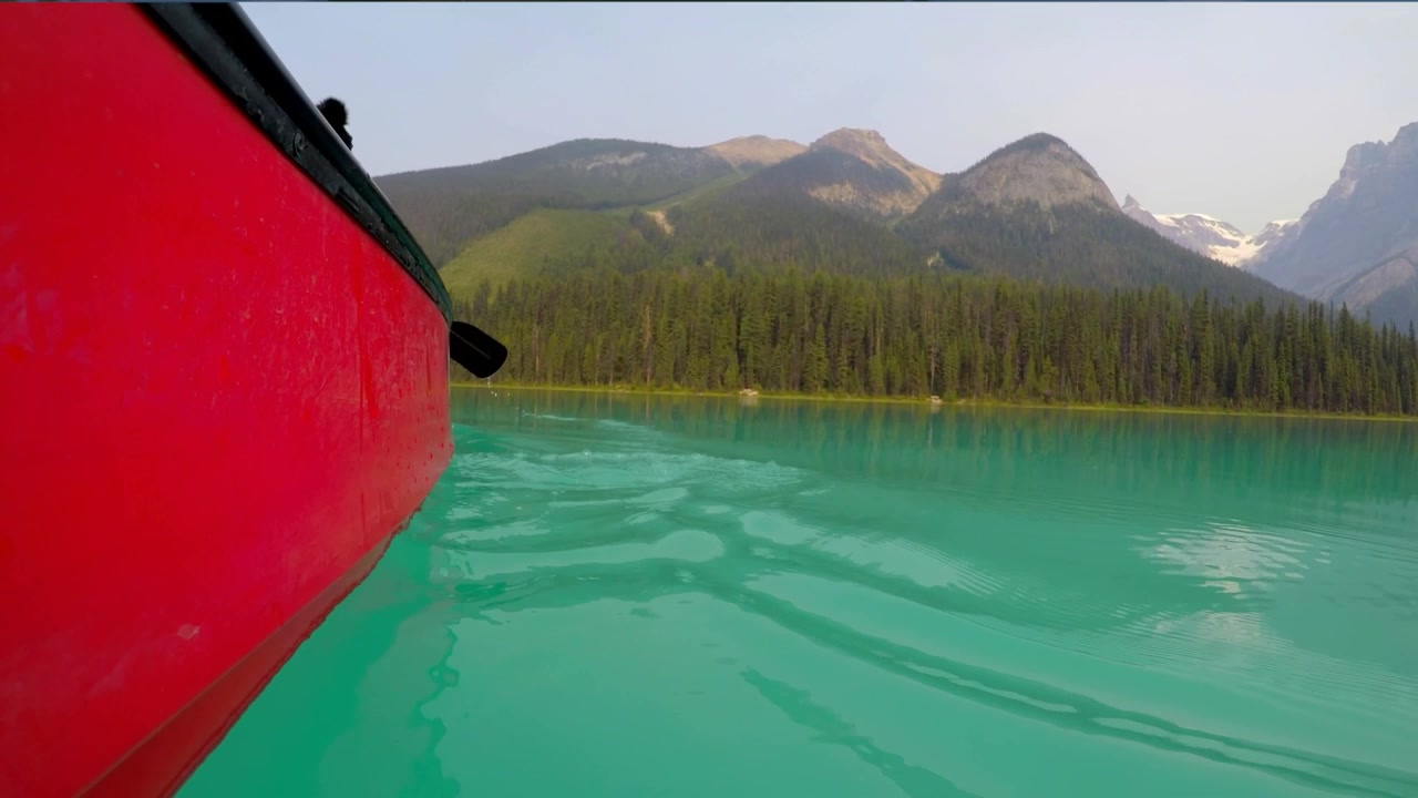 Person paddelt in einem roten Kanu auf einem türkisfarbenen Bergsee