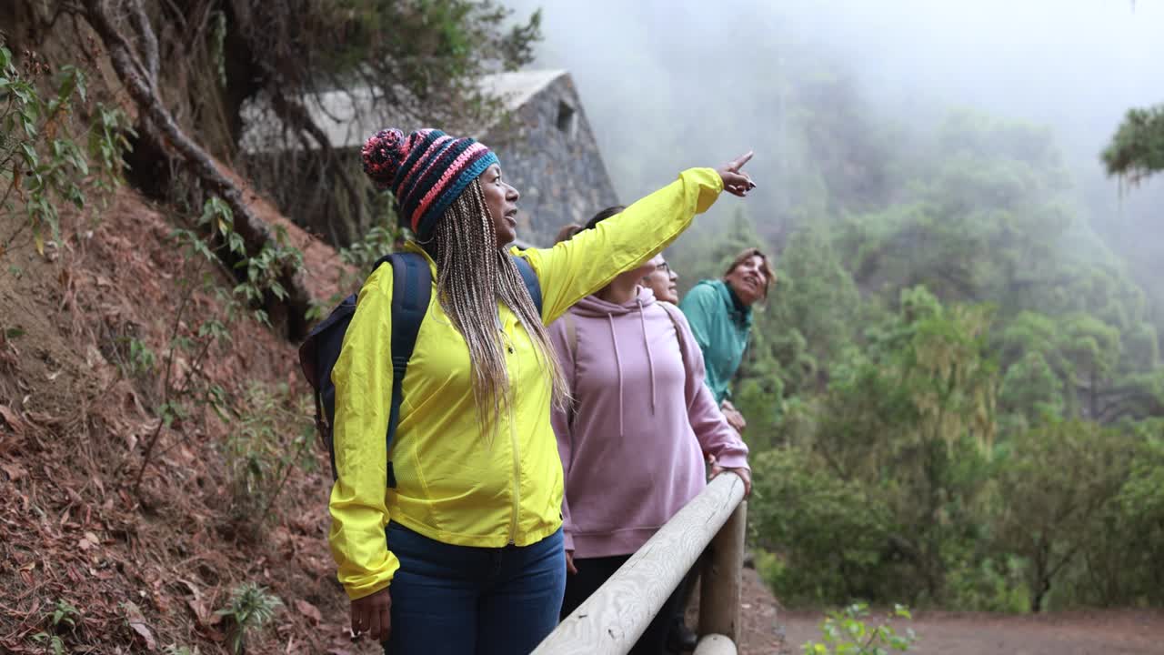 mujeres multirraciales divirtiéndose durante el día de senderismo en el bosque con casa de piedra en el fondo