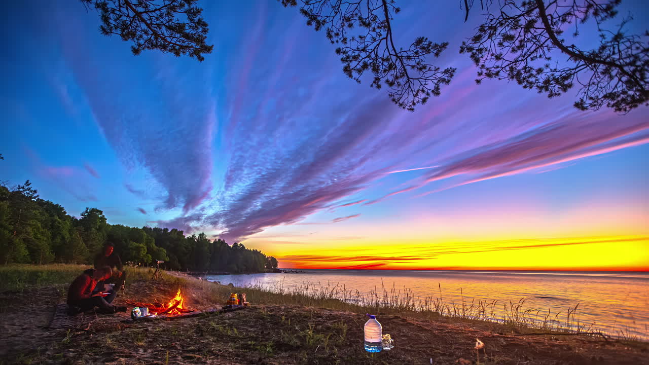 люди в лагере с кострами у заката на пляже