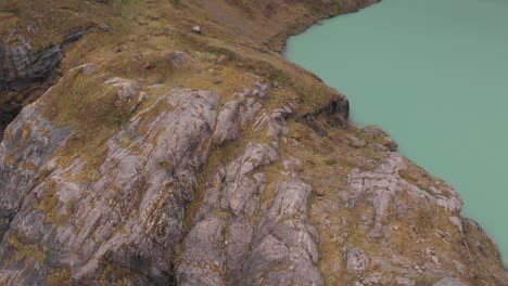 Flying-Over-Quilotoa-Lagoon,-Rocky-Mountain-Edge-Of-Greenish-Volcanic-Crater-Lake